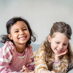 Two smiling kids enjoying creative play with a Christmas-themed bracelet-making kit, perfect for children aged 4 and above.