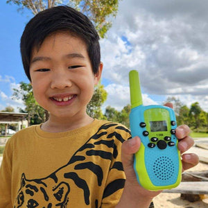 Child holding a blue and green kids walkie talkie outdoors on a sunny day