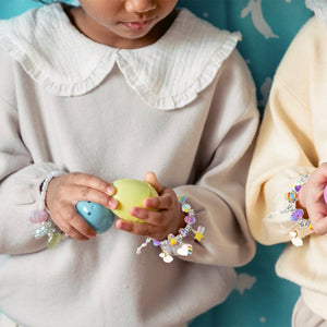Child wearing colorful charm bracelets made with a kids bracelet-making kit, holding plastic eggs.