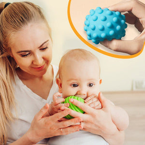 Baby playing with textured sensory balls from Busy Board Montessori educational toy set with mother assisting.